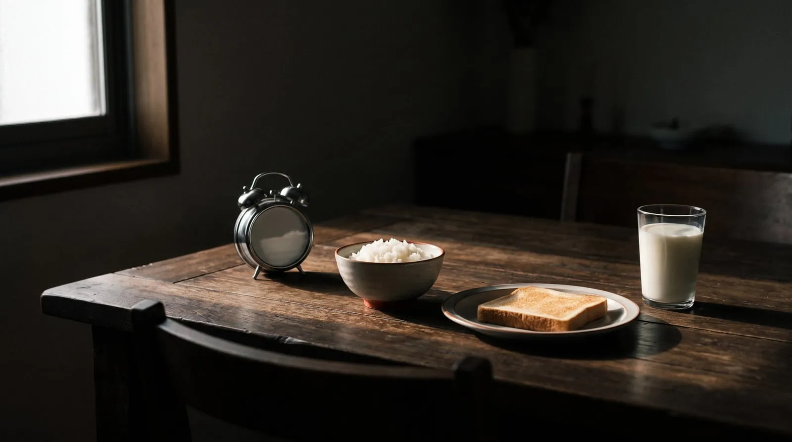 朝日が差し込むダイニングテーブルに置かれた目覚まし時計とご飯茶碗、トーストの皿が並ぶ静物