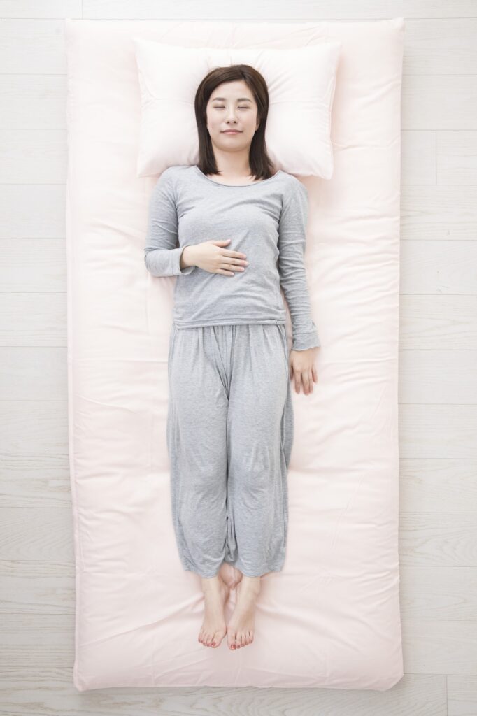 布団の上に仰向けで目を閉じている女性